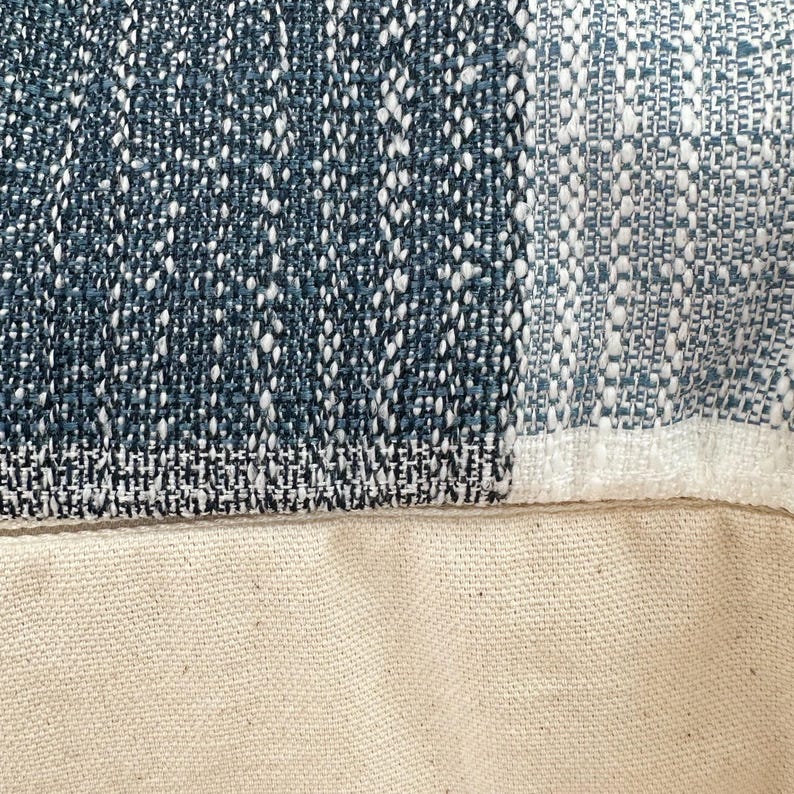 May include: Close-up of a blue and white patterned fabric with a white canvas backing. The fabric has a woven texture and a geometric design.