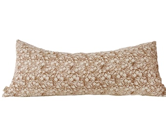 Puede incluir: Una almohada larga y rectangular con un estampado floral marrón y blanco. La almohada está hecha de una tela suave y cómoda y es perfecta para añadir un toque de estilo a cualquier habitación.