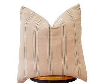 May include: A striped throw pillow with a beige background and thin black stripes. The pillow is sitting on a wooden stool.