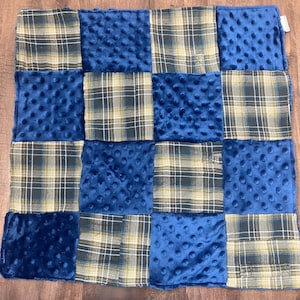May include: A square patchwork blanket with alternating squares of blue minky fabric and plaid flannel. The plaid incorporates shades of blue, green, and beige. The blanket is designed with a grid pattern, creating a visually appealing texture.
