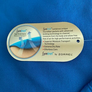 May include: A close-up of a blue fabric tag with the text "Syntrel&trade;" and a description of the fabric's moisture-wicking properties. The tag also includes the text "by ZORREL".