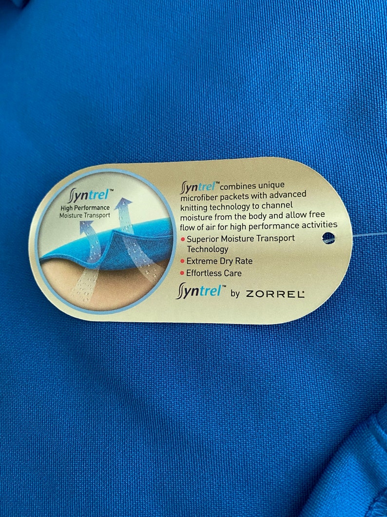 May include: A close-up of a blue fabric tag with the text "Syntrel&trade;" and a description of the fabric's moisture-wicking properties. The tag also includes the text "by ZORREL".