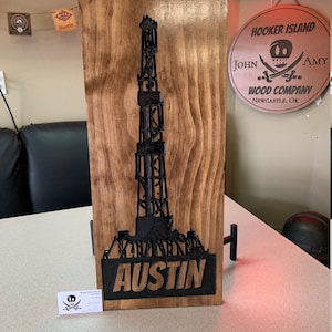 May include: A wooden sign with a black silhouette of an oil rig and the name "Austin" carved into the wood. The sign is mounted on a wooden stand. The sign is made by Hooker Island Wood Company in Newcastle, Oklahoma.