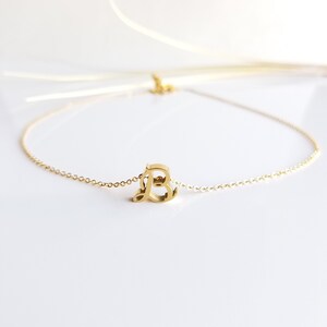 May include: A gold chain necklace with a cursive letter 'B' pendant.