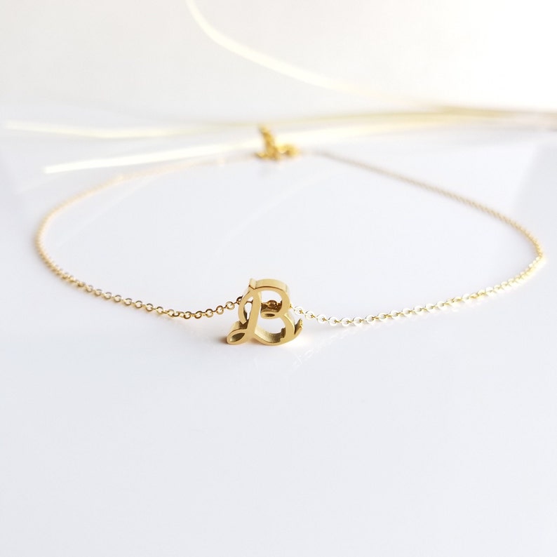 May include: A gold chain necklace with a cursive letter 'B' pendant.