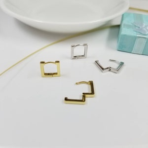 May include: Three pairs of square hoop earrings. One pair is gold, one pair is silver, and one pair is silver with a zig-zag design.