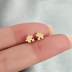 May include: A pair of gold-toned puzzle piece stud earrings. The earrings are small and delicate, and they are perfect for everyday wear.