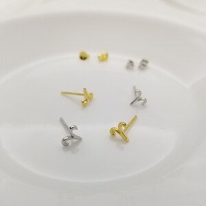 May include: A set of four gold and silver stud earrings featuring a stylized swirl design. The earrings are displayed on a white surface.
