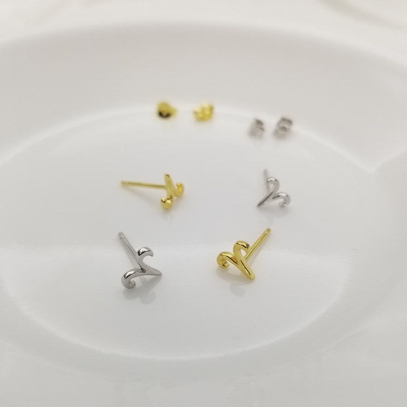 May include: A set of four gold and silver stud earrings featuring a stylized swirl design. The earrings are displayed on a white surface.