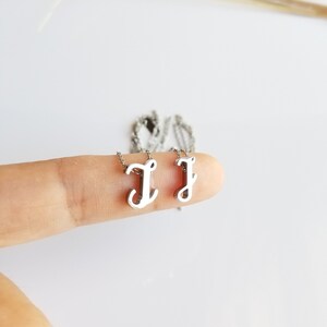 May include: Two silver necklaces with a cursive letter J pendant. The necklaces are on a finger.