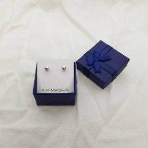 May include: A pair of silver ball stud earrings in a blue gift box with a blue ribbon. The box has the text "LittleSilverjeweler" printed on it.