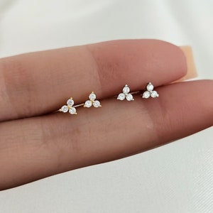 May include: A pair of small, gold and silver earrings with three clear cubic zirconia stones each, arranged in a triangular shape.