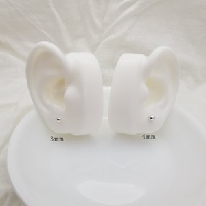 May include: Two white ear models with silver stud earrings. The left ear model has a 3 mm stud and the right ear model has a 4 mm stud.