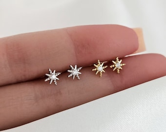 May include: Three pairs of star-shaped earrings with a small clear stone in the centre. The earrings are in silver, gold, and rose gold.