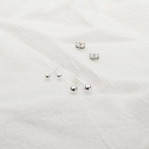 May include: Three pairs of silver stud earrings with small round balls. The earrings are on a white surface.