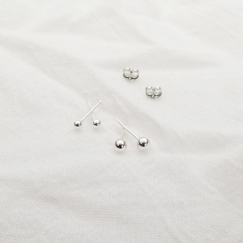 May include: Three pairs of silver stud earrings with small round balls. The earrings are on a white surface.