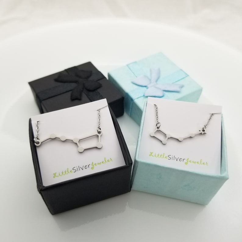 May include: Two small gift boxes with a silver constellation necklace inside each. The boxes are black and light blue with a white interior. The necklaces are on a white card with the text "LittleSilverJeweler" printed on them.