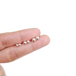 May include: A set of five silver ball stud earrings of varying sizes, displayed on a finger.