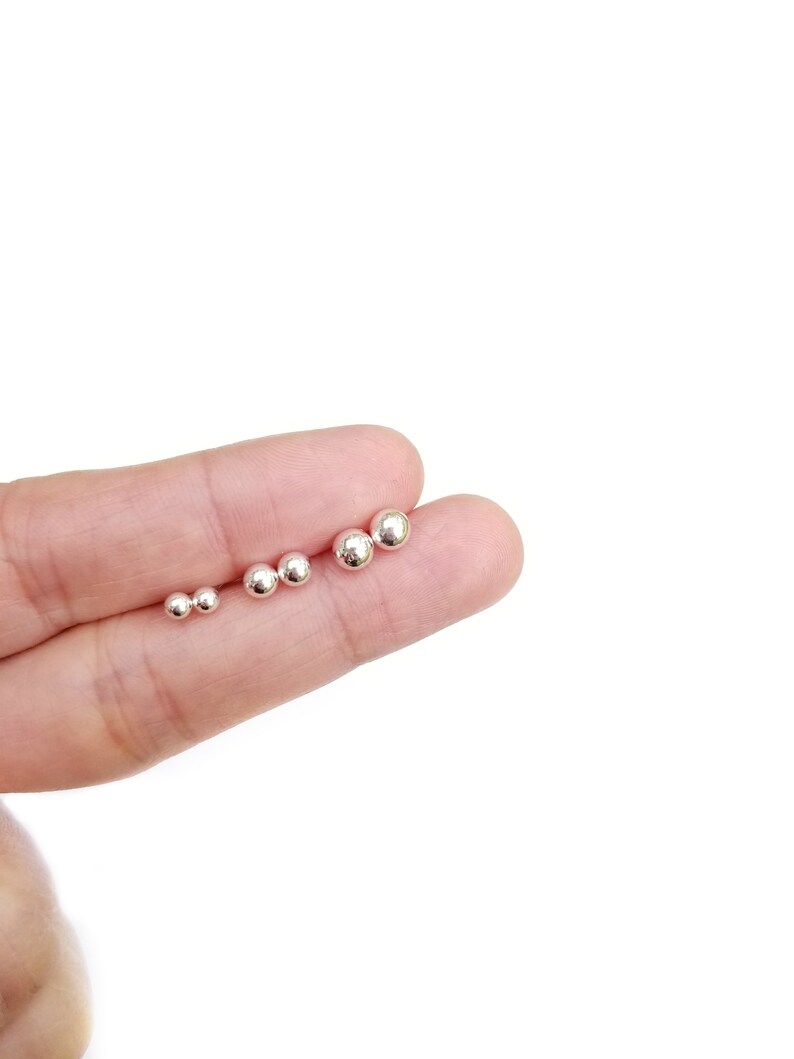 May include: A set of five silver ball stud earrings of varying sizes, displayed on a finger.