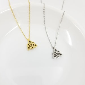 May include: Two delicate necklaces with a Celtic knot pendant. One necklace is gold and the other is silver. The necklaces are displayed on a white plate.