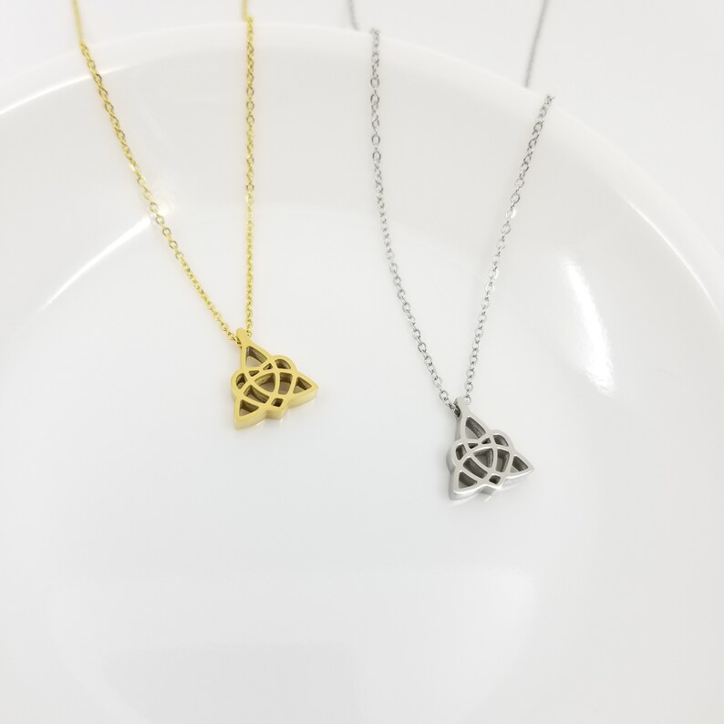 May include: Two delicate necklaces with a Celtic knot pendant. One necklace is gold and the other is silver. The necklaces are displayed on a white plate.