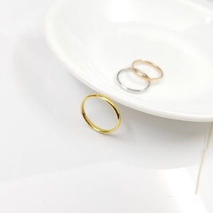May include: Three thin, simple, metal rings in gold, silver, and rose gold. The rings are stacked on top of each other on a white surface.
