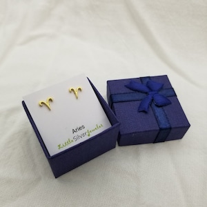 May include: Gold Aries zodiac sign stud earrings in a blue gift box with a blue ribbon and bow. The box has the text "LittleSilverJeweler" on it.
