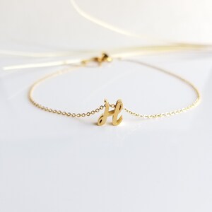 May include: A gold chain bracelet with a cursive letter 'H' charm.