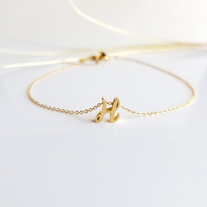 May include: A gold chain bracelet with a cursive letter 'H' charm.