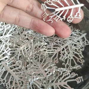 May include: A close-up of a pile of silver zodiac sign charms. The charms are in the shape of the twelve astrological signs. The charms are arranged in a random order.