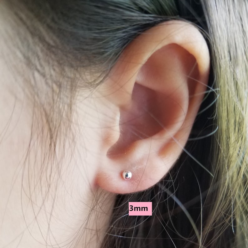 May include: Close-up of a person's ear with a small, silver stud earring. The earring is 3mm in diameter.