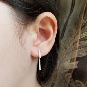 May include: A pair of silver dangle earrings with a small bar at the top and a longer bar with small clear stones hanging from it.