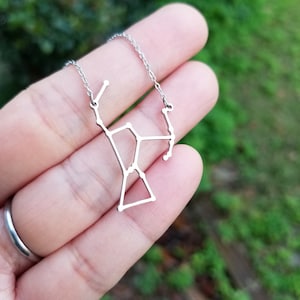 May include: A silver necklace with a constellation pendant. The pendant is a delicate outline of a constellation, possibly Ursa Major.