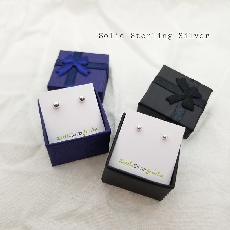 May include: Two pairs of sterling silver stud earrings in small gift boxes. The boxes are blue and black with a ribbon and bow. The text "Solid Sterling Silver" is at the top of the image. The text "Little Silver Jeweler" is on the bottom of each box.