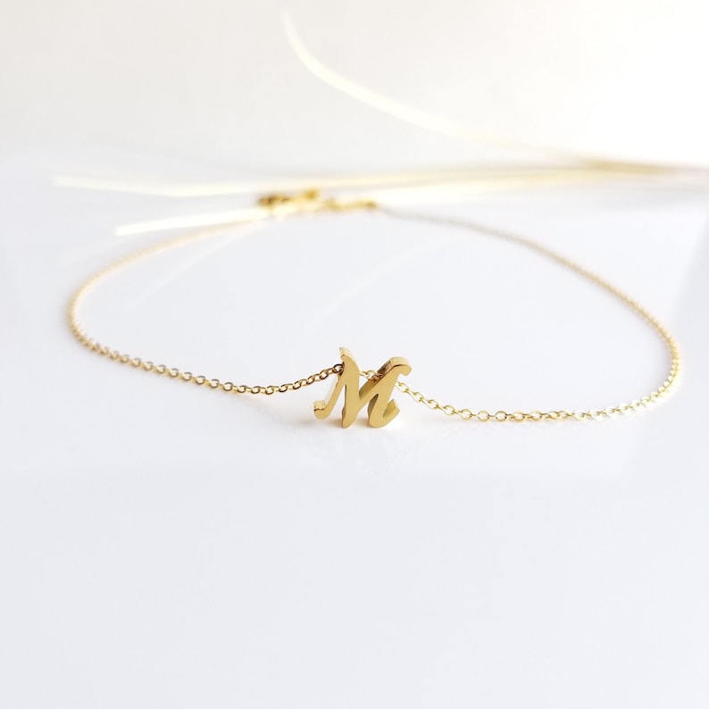 May include: A gold chain necklace with a cursive letter 'M' pendant.