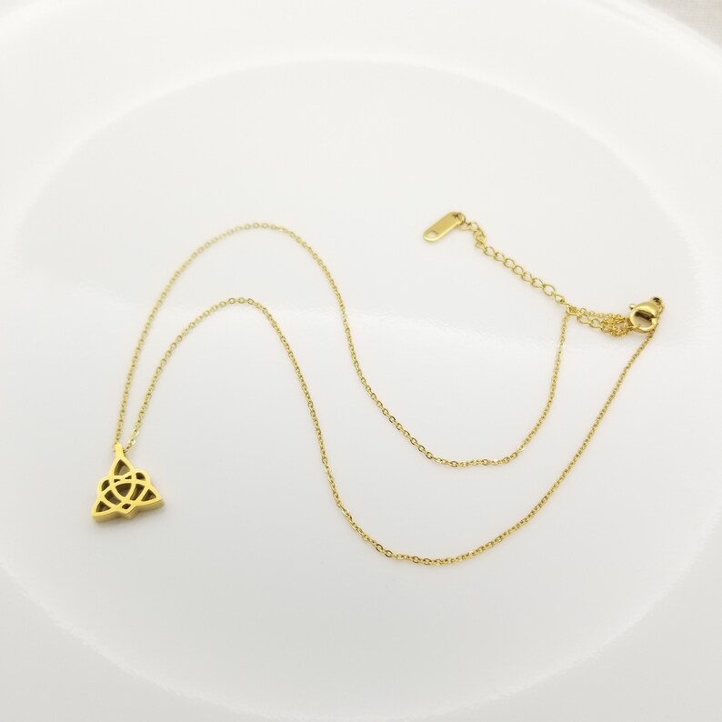 May include: A gold-toned necklace with a Celtic knot pendant. The chain is a delicate, thin chain.