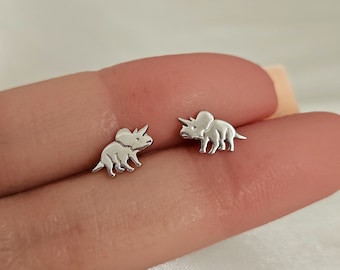 May include: A pair of silver earrings featuring a small, detailed triceratops design.