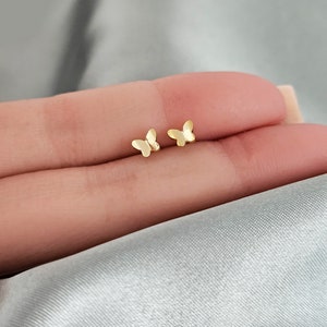 May include: A pair of gold butterfly stud earrings. The earrings are small and delicate, and they are perfect for everyday wear.
