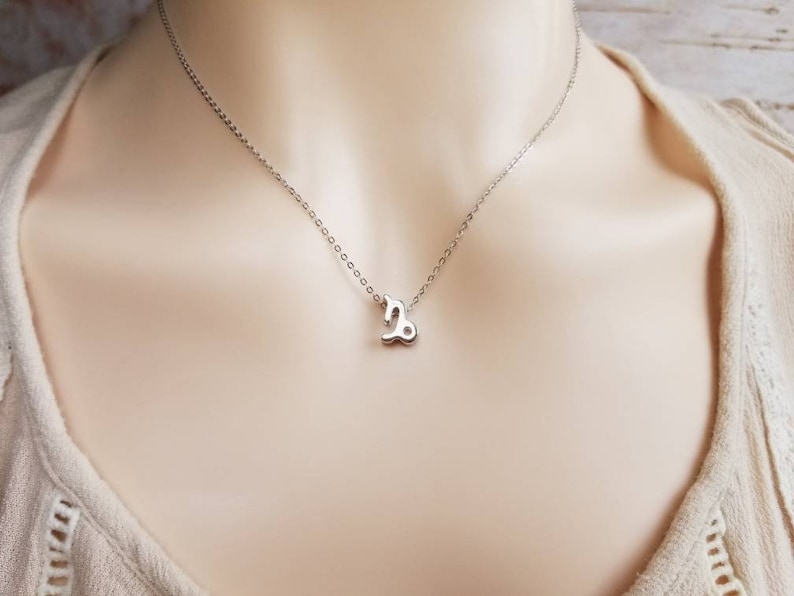 May include: A silver necklace with a small, silver Capricorn zodiac symbol pendant.