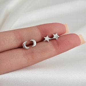 May include: A set of three silver earrings featuring a crescent moon and two stars.