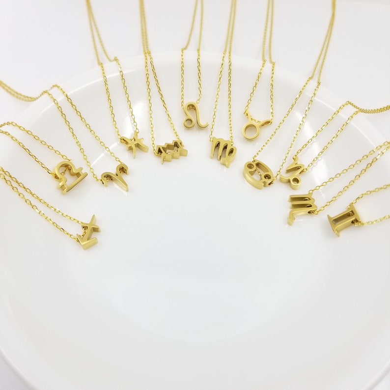 May include: A set of 12 gold zodiac necklaces on a white plate. Each necklace features a different zodiac symbol.