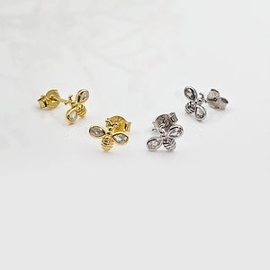 May include: Three pairs of bee stud earrings with clear cubic zirconia stones. The earrings are available in gold, silver, and rose gold.
