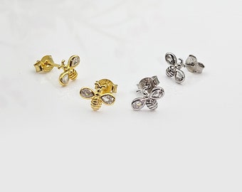 May include: Three pairs of bee stud earrings with clear cubic zirconia stones. The earrings are available in gold, silver, and rose gold.