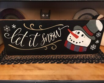 May include: A black wooden box with the words "let it snow" in white script. A snowman with a red scarf, carrot nose, and top hat is painted on the right side. White snowflakes are also painted on the box.