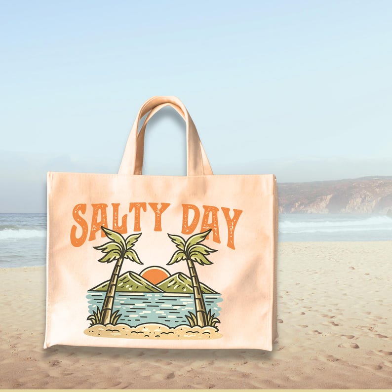 Pu&ograve; includere: Una borsa tote color pesca con le parole "SALTY DAY" in arancione. La grafica presenta due palme, una montagna e un sole al tramonto sull'acqua. La borsa ha due manici ed &egrave; su una spiaggia sabbiosa.