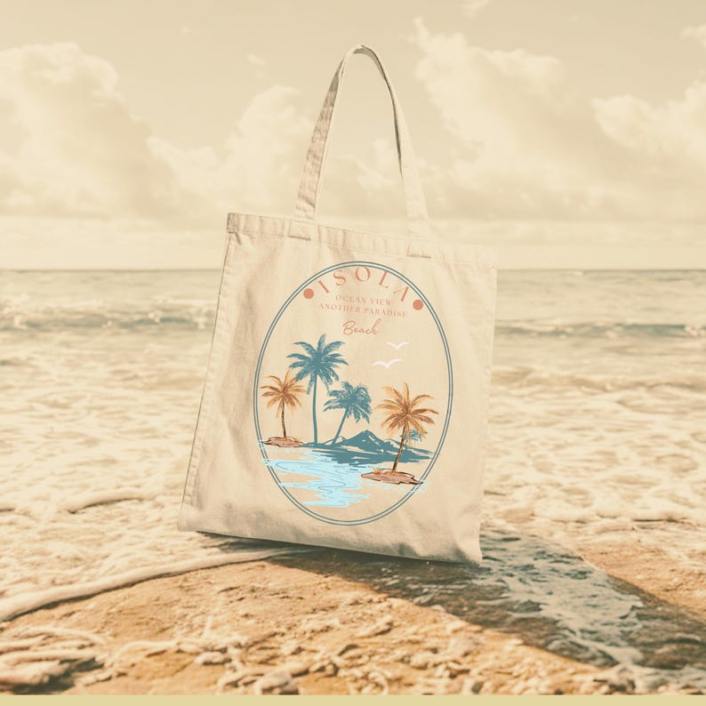 Pu&ograve; includere: Borsa tote beige con una scena di spiaggia tropicale. Il design presenta palme, acqua e le parole "ISOLA Ocean View Another Paradise Beach" in una cornice circolare. La borsa ha un lungo manico.