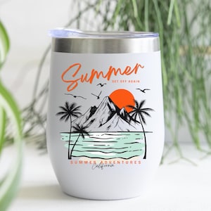 Pu&ograve; includere: Bicchiere da vino isolato bianco con bordo e coperchio argentati. Il bicchiere presenta una grafica di un tramonto sulle montagne, palme e la parola "Summer" in scrittura arancione. Il testo in basso recita "Summer Adventures California."