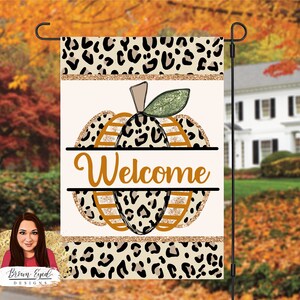 May include: A welcome garden flag with a leopard print pumpkin design. The pumpkin is orange and brown with gold glitter accents. The text "Welcome" is in orange.
