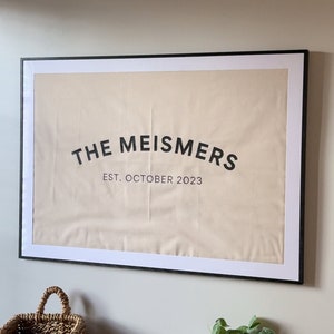 May include: A framed canvas print with the text "THE MEISMERS EST. OCTOBER 2023" in black lettering on a beige background.