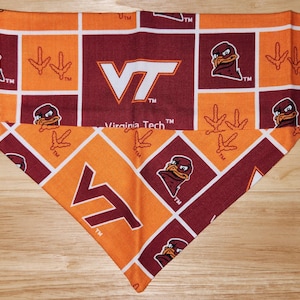 May include: A maroon and orange bandana with a repeated pattern of the Virginia Tech logo, a bird mascot, and a three-toed footprint. The bandana is folded into a triangle shape. "Virginia Tech" is printed on the bandana.